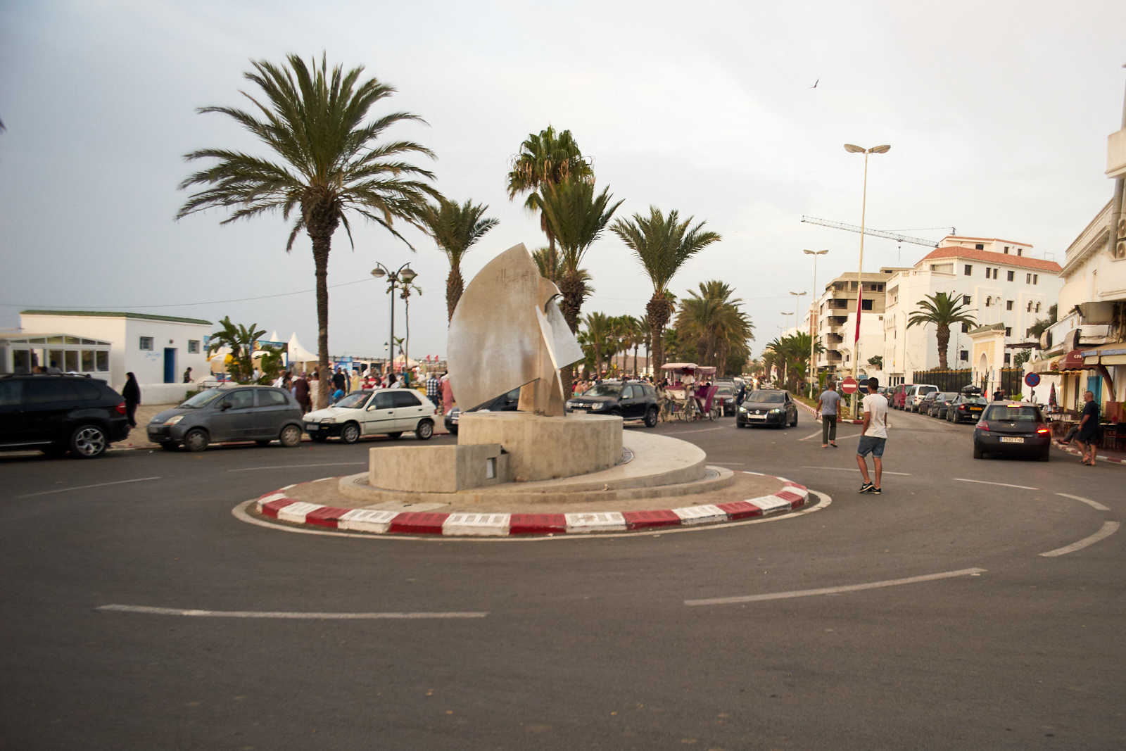 Rond-point à Asilah avec une sculpture, des palmiers et des immeubles