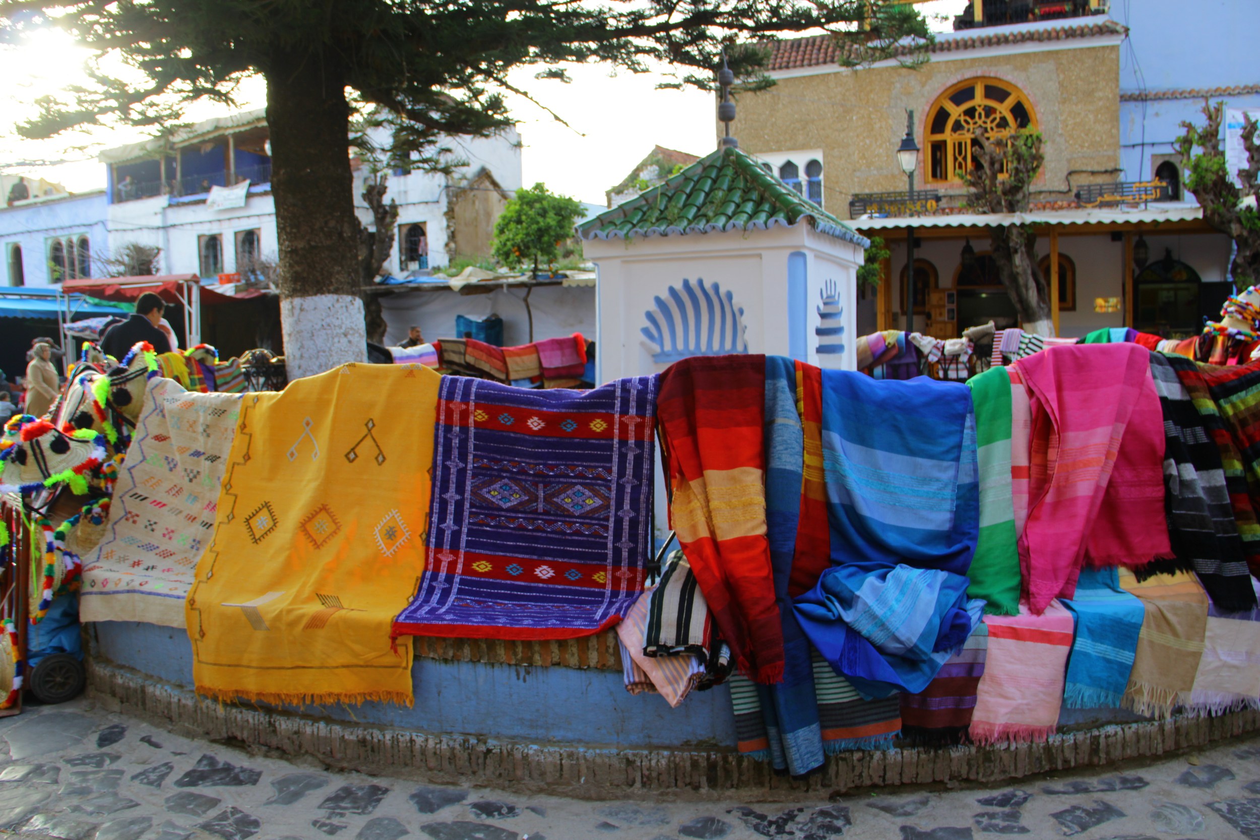 Tissus et tapis colorés exposés autour d'une place du centre de Chefchaouen