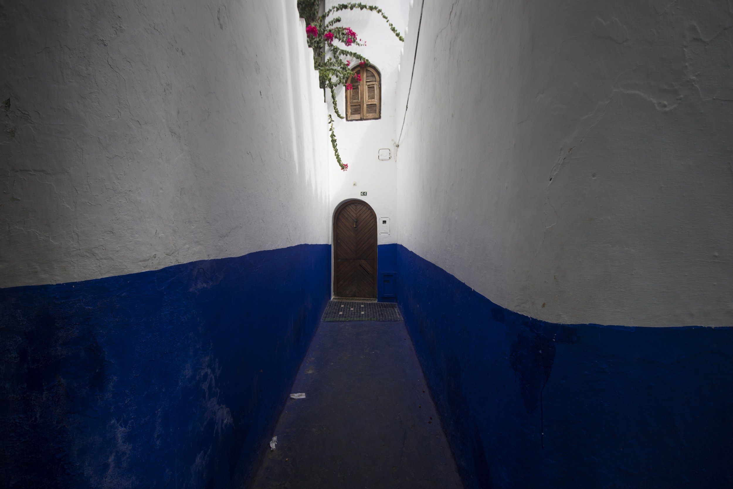 Ruelle étroite aux murs blancs et bleus à Chefchaouen, avec une porte au fond