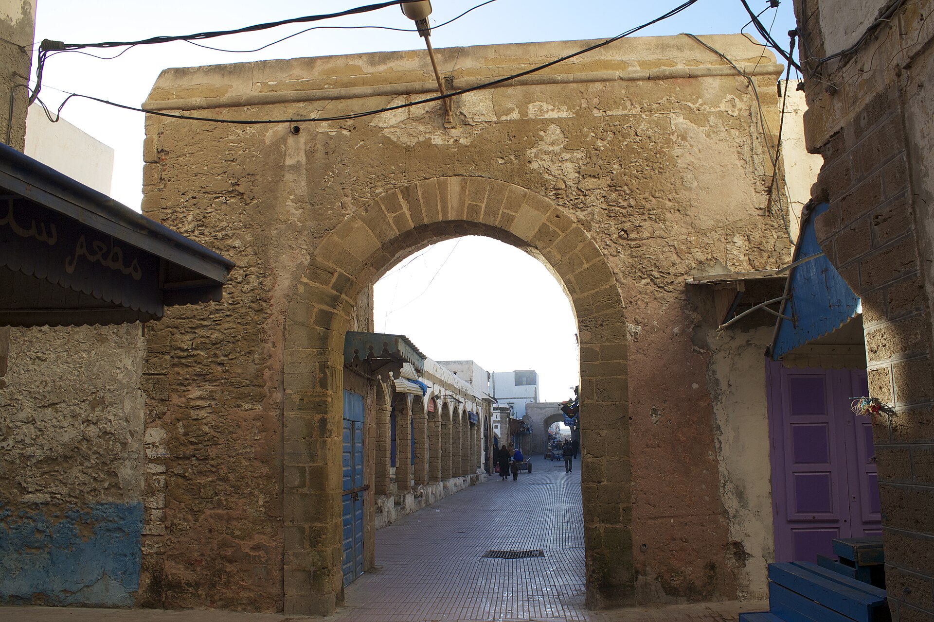 Rue de la médina d'Essaouira passant sous une arche de pierre, à l'entrée nord-ouest du Souk Jdid.
