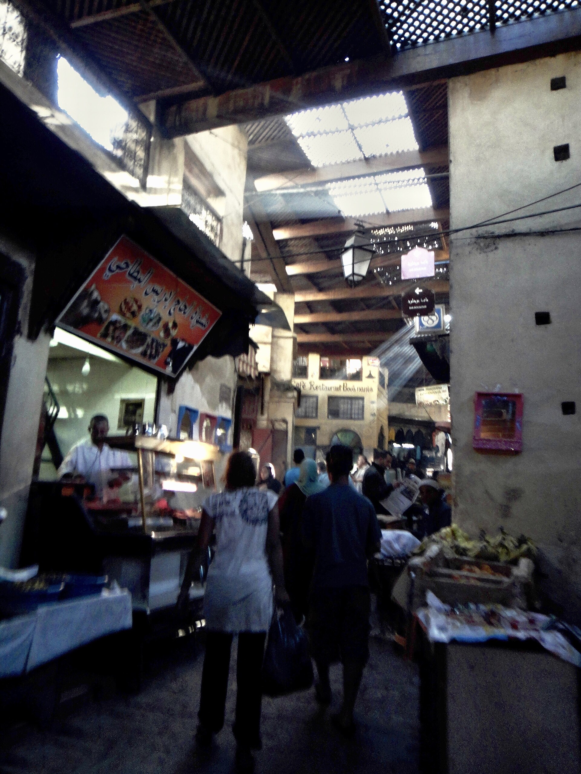 Ruelle commerçante de la Talaa dans la médina de Fès, avec étals et passants.