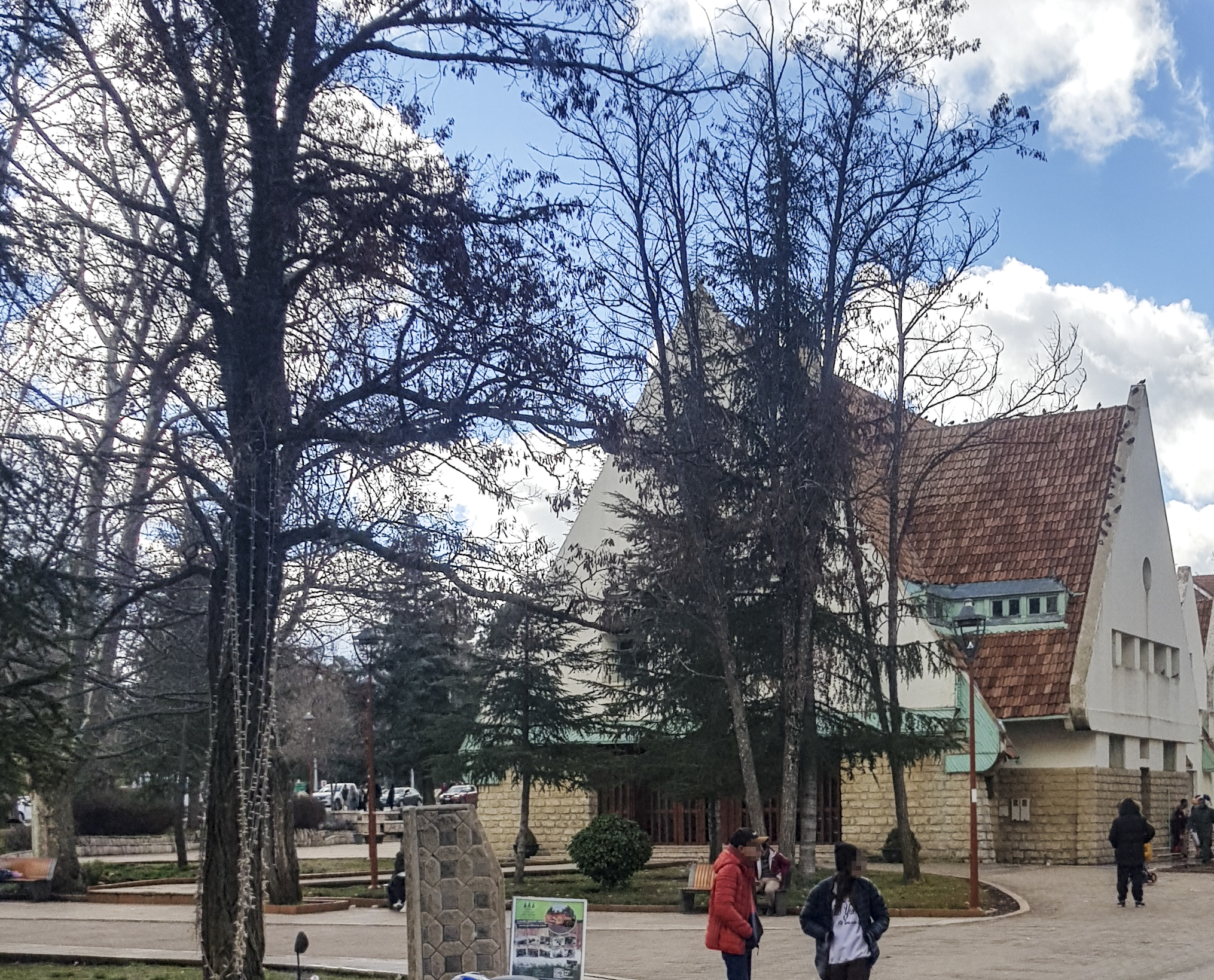 Centre-ville d'Ifrane avec une maison à toit de tuiles rouges et des passants sous les arbres