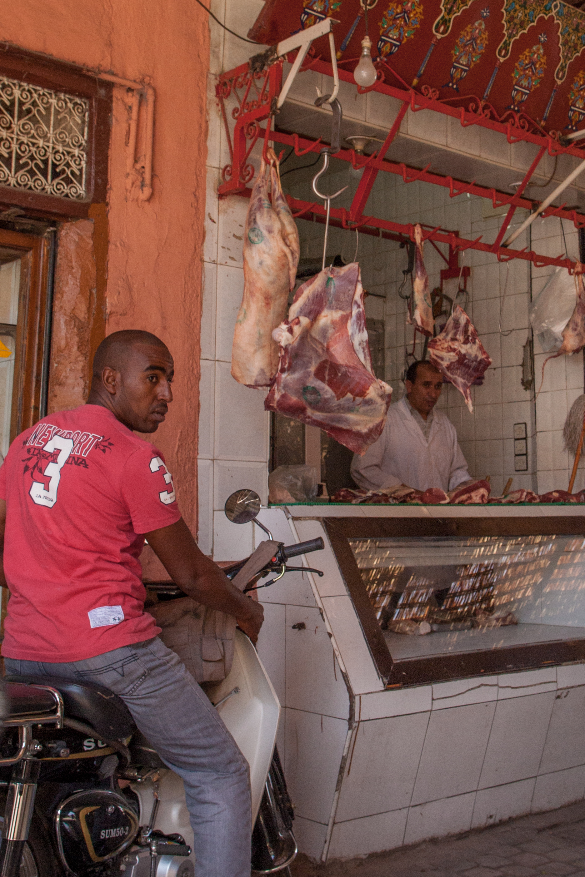Scène de rue dans la médina de Marrakech : un boucher dans sa boutique et un habitant sur son scooter.