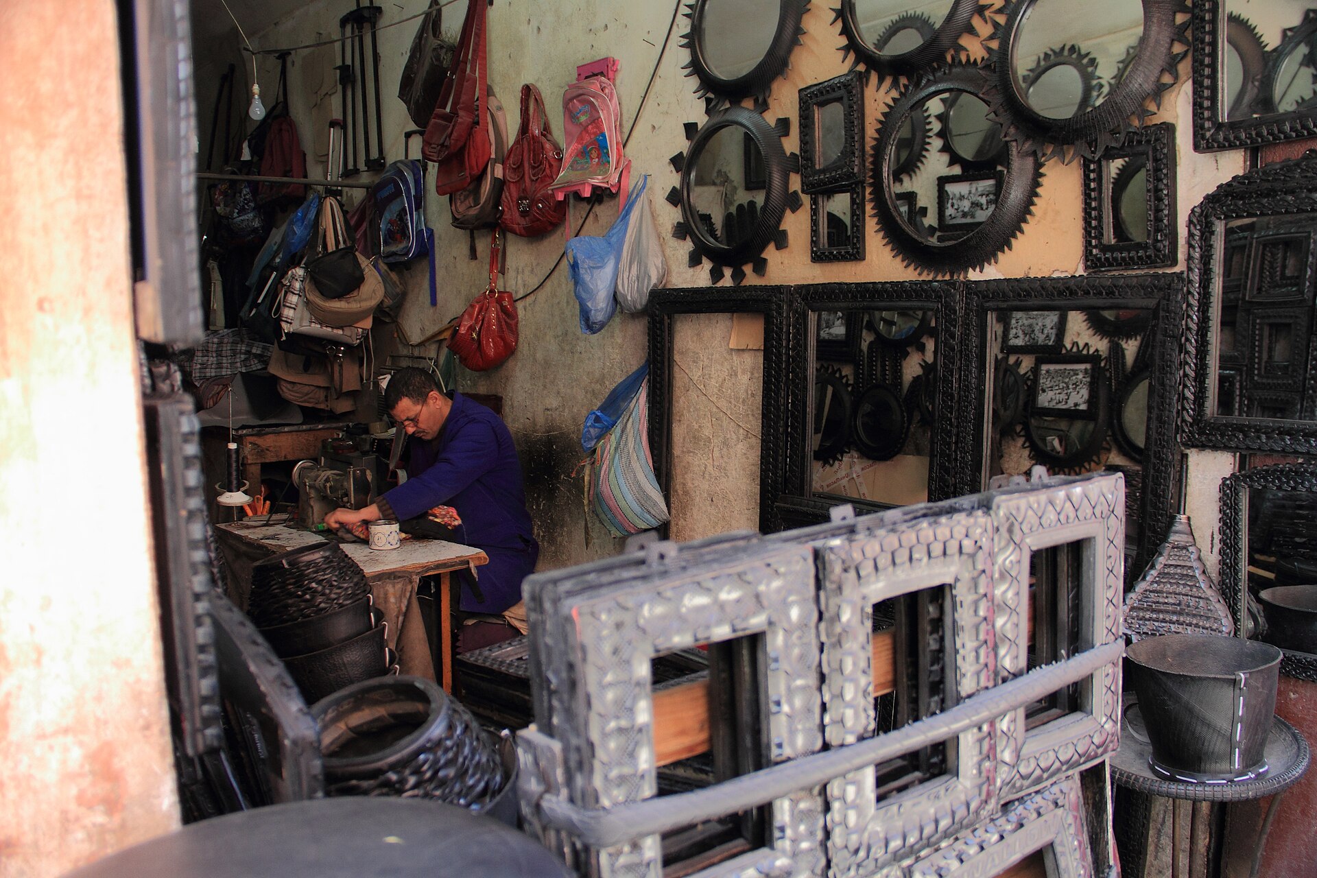 Artisan travaillant dans son échoppe du souk de Marrakech, entouré de miroirs et d'objets en métal recyclé.