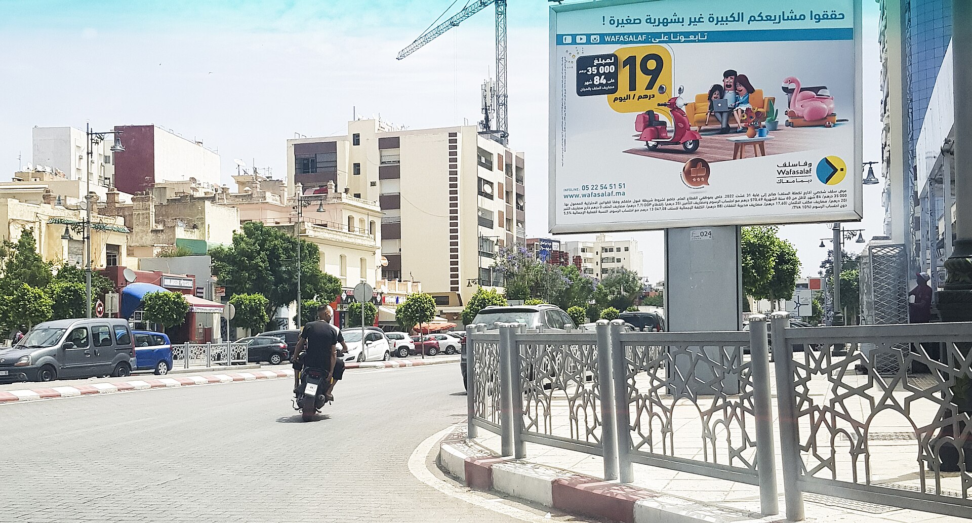 Rue et immeubles du quartier Hamria à Meknès, avec circulation et panneau publicitaire.