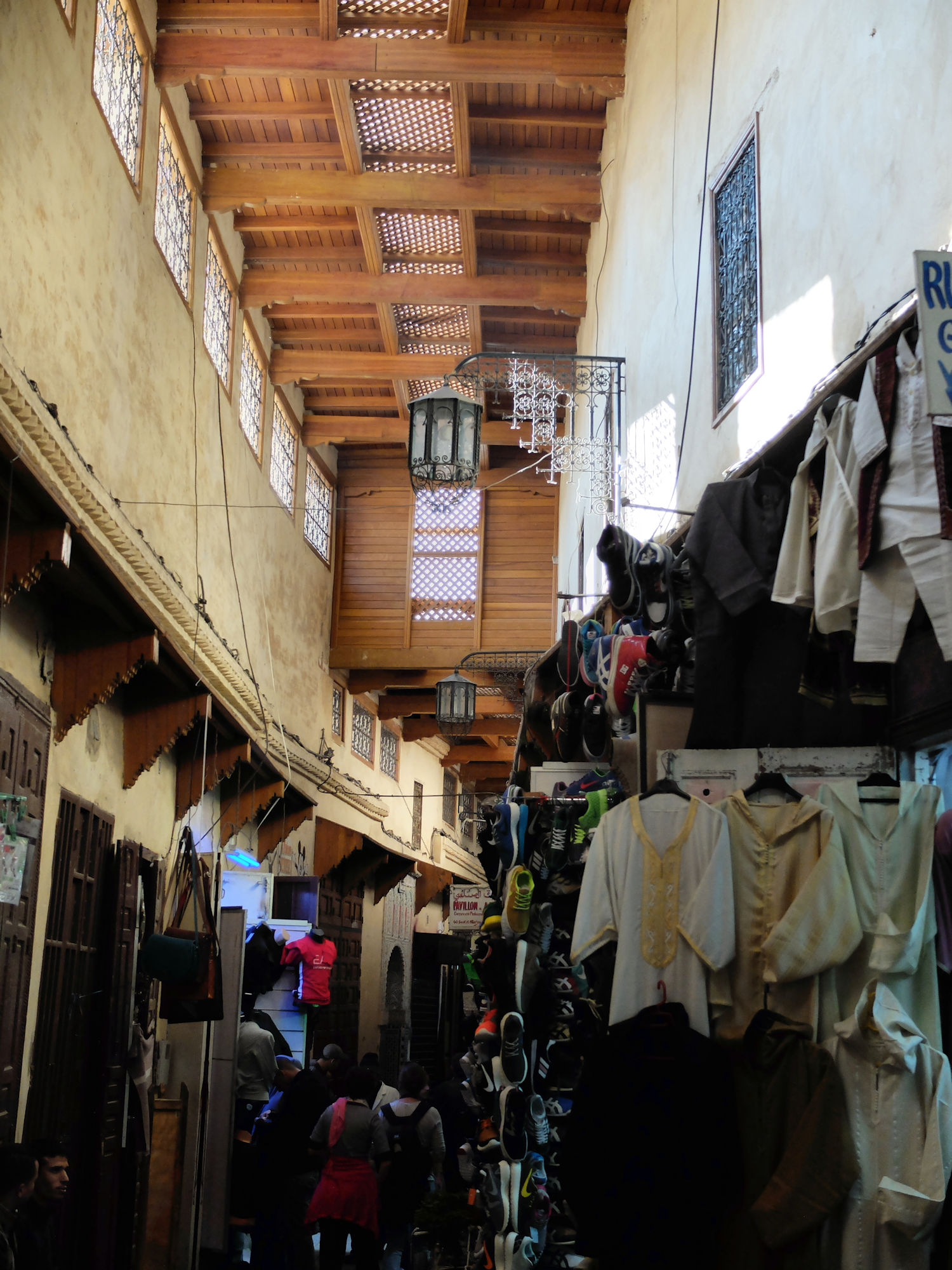 Ruelle couverte d'un souk de la médina de Meknès, avec vêtements en vente et passants.