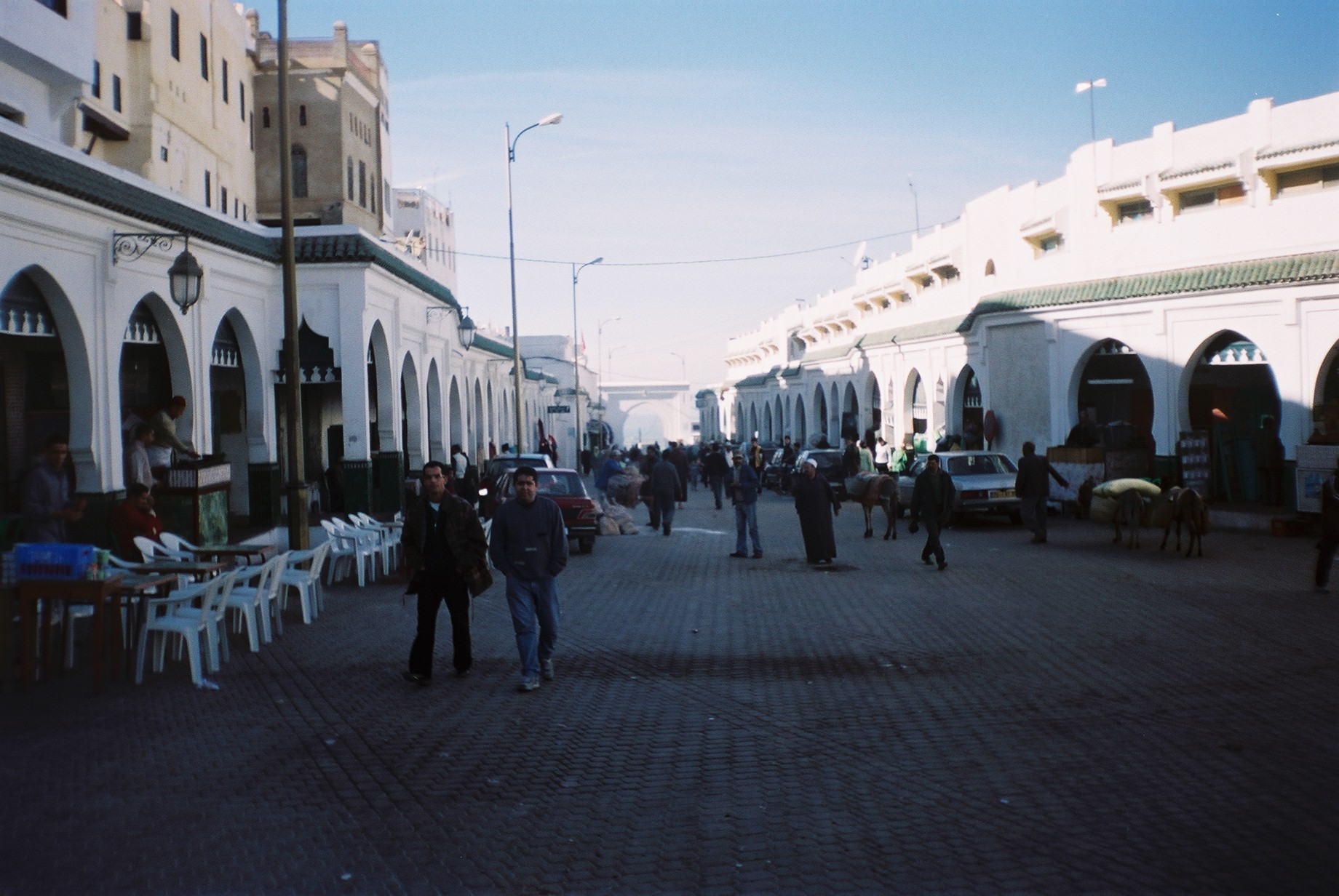 Rue piétonne bordée d'arcades blanches à Moulay Idriss, avec des passants et des terrasses